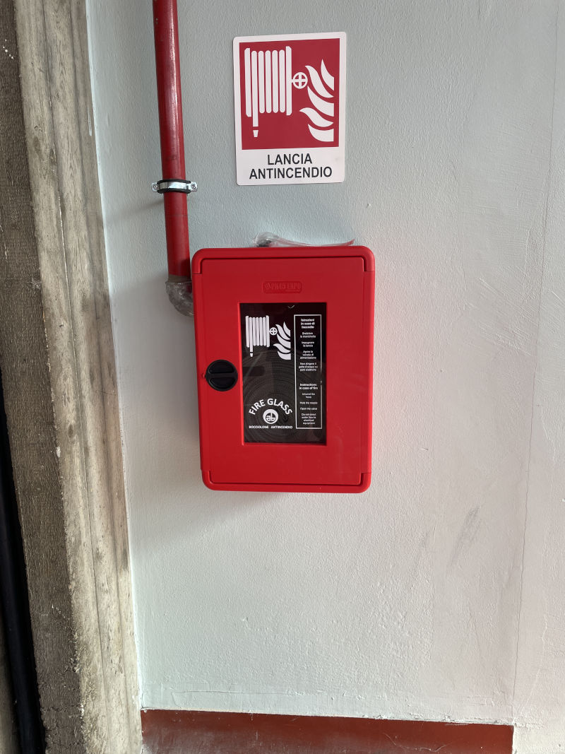 Cassetta antincendio a parete con segnaletica per lancia antincendio e tubazione di alimentazione rossa.