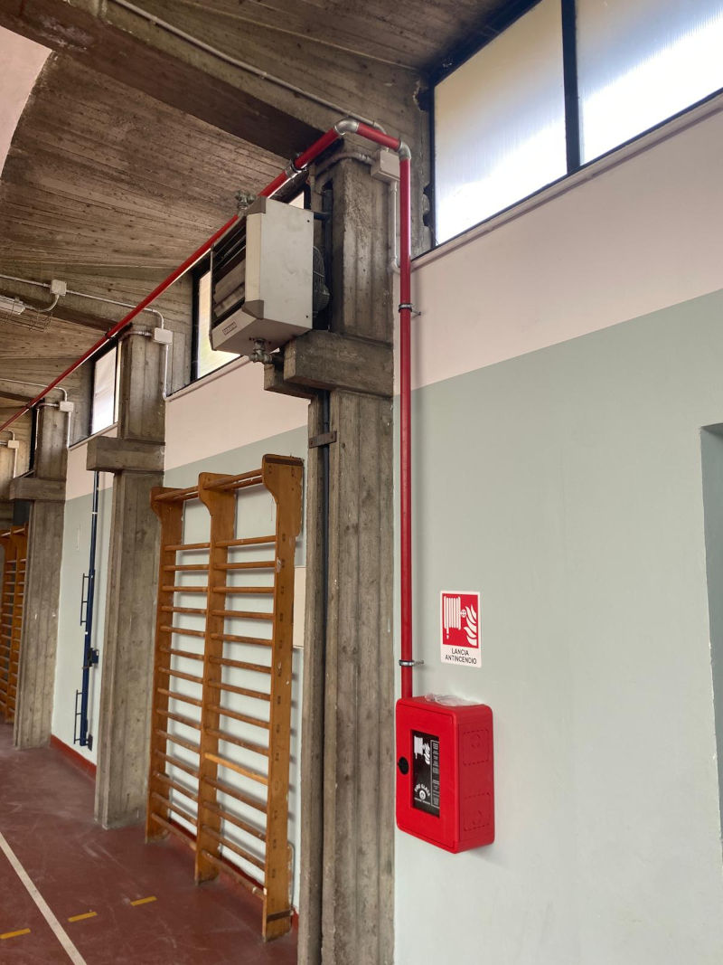 Impianto antincendio con tubazioni rosse a vista e cassetta per idrante a muro UNI 45 in un edificio industriale.